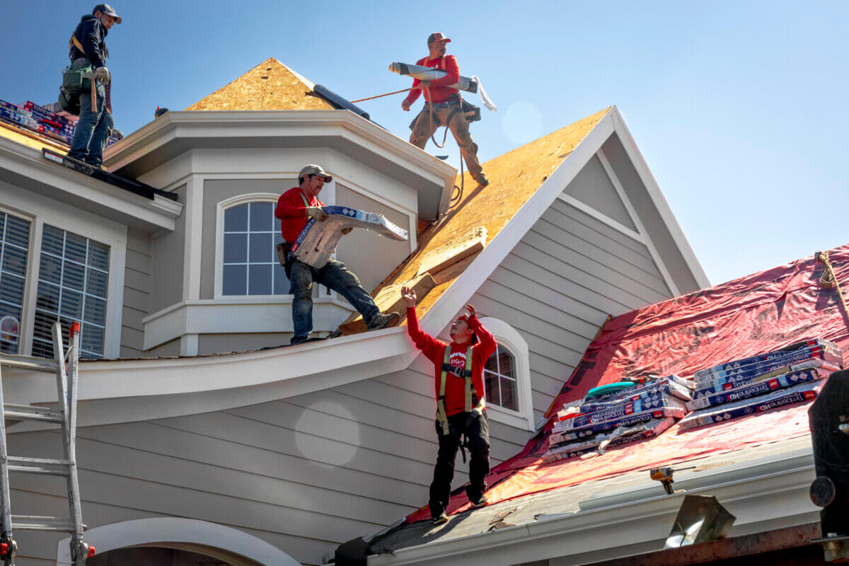 PRQ crew tearing off an old roof and carrying new shingle bundles up the slope